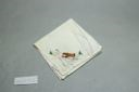 Image of Figure with miniature boat, one of a set of 2 embroidered napkins with scenes of Inuit figure at play